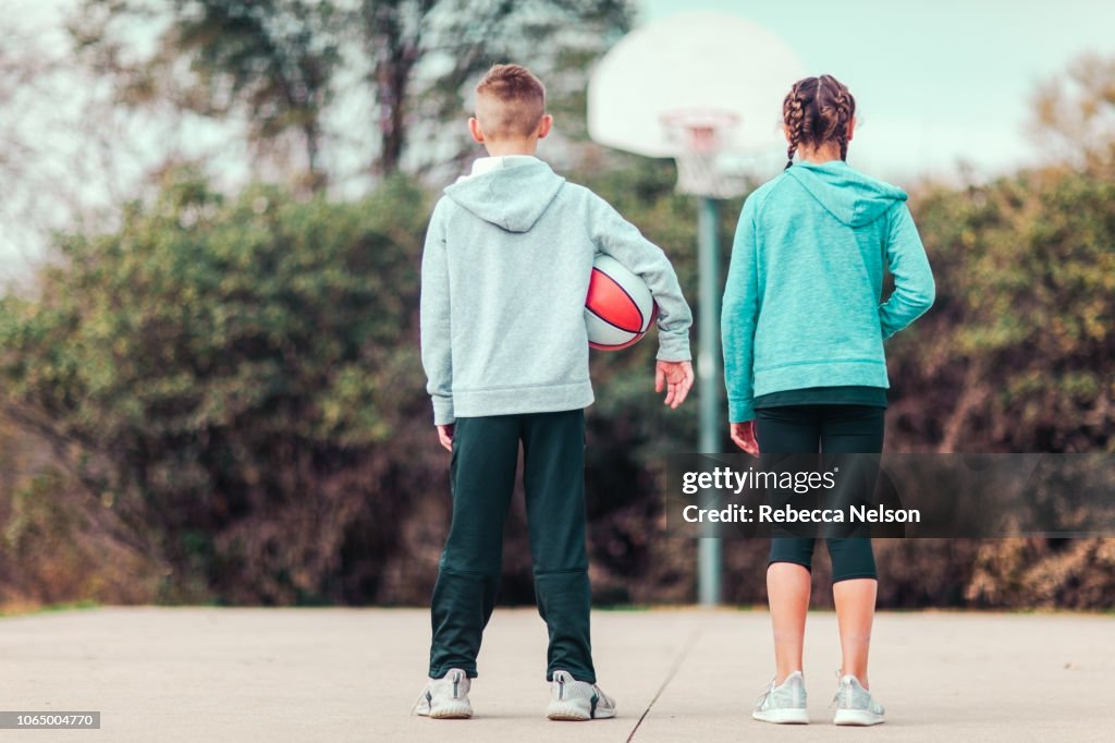 Pre-teen boy and girl playing basketball on the playground