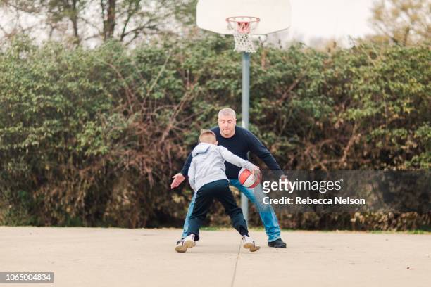 pre-teen son and father playing basketball on playground - blocking sports activity stock pictures, royalty-free photos & images