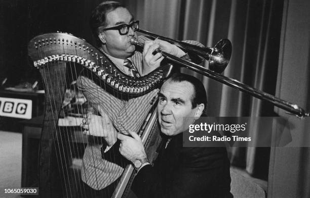 Broadcaster John Amis playing the trombone as musician Ian Wallace plays the harp, photographed for Radio Times in connection with the BBC Radio 4...