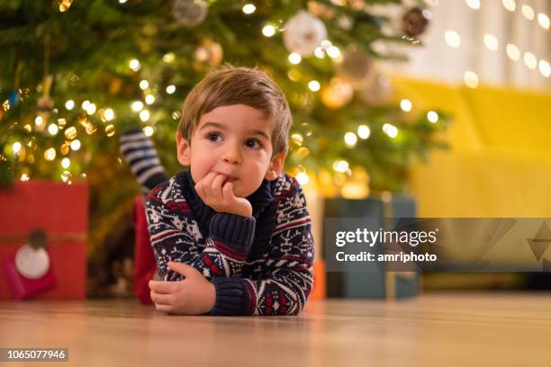 niño pensativo bajo el árbol de navidad - children thinking fotografías e imágenes de stock