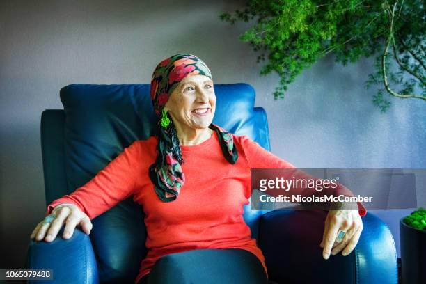 vibrant senior woman wearing a head scarf smiling in her living room - recliner chair stock pictures, royalty-free photos & images