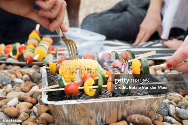 close up of hands preparing food on disposable barbecue on pebble beach. - disposable silverware stock pictures, royalty-free photos & images