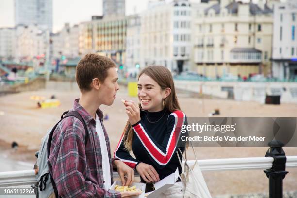 teenager gives chip to boyfriend standing on promenade. - young couple beach stock pictures, royalty-free photos & images