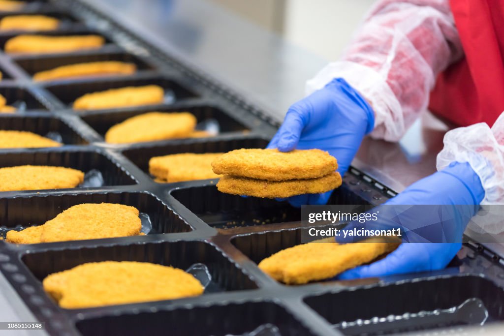 The worker in the factory places the chicken schnitzel