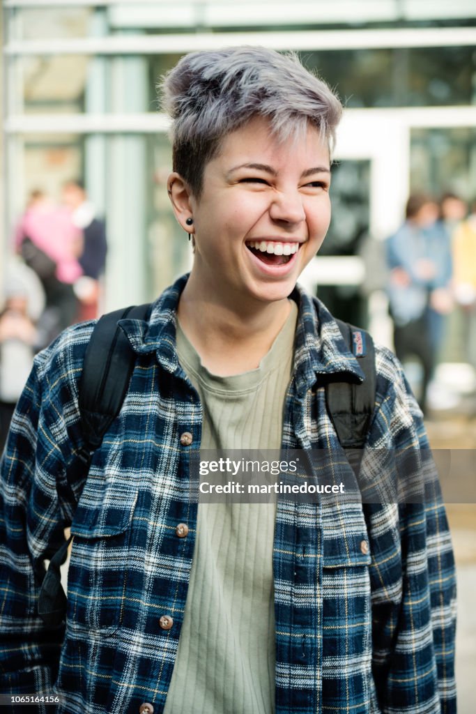 Portrait of non-binary gender young adult student in front of College.