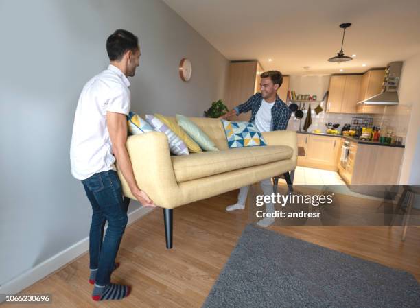 happy homosexual couple moving the furniture at home - gay couple new house stock pictures, royalty-free photos & images