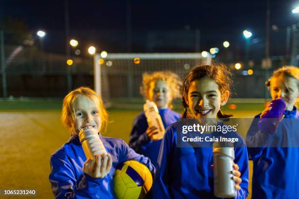 portrait smiling girls soccer team taking a break from practice, drinking water on field at night - football team stock pictures, royalty-free photos & images