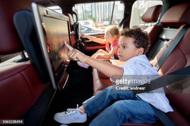 happy kids watching television in a car while wearing their seat belt fastened - child car tablet stock pictures, royalty-free photos & images