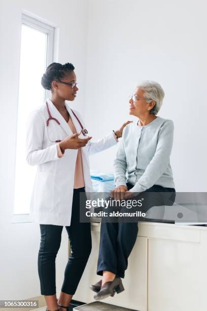senior female patient consulting with young female doctor - hispanic medical exam stock pictures, royalty-free photos & images