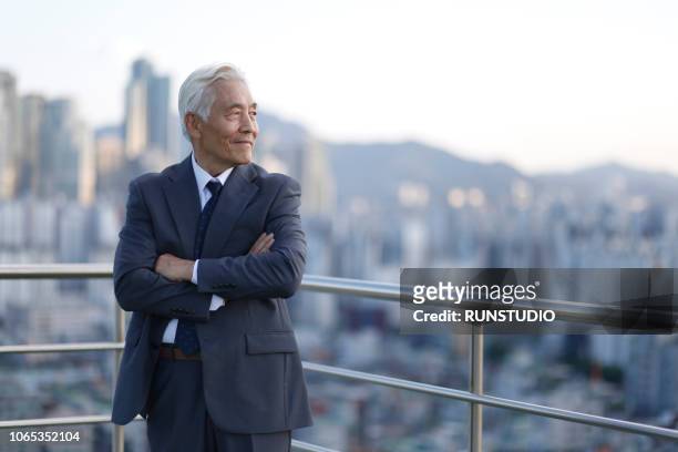 senior businessman standing with arms crossed on rooftop - chief executive officer stock-fotos und bilder