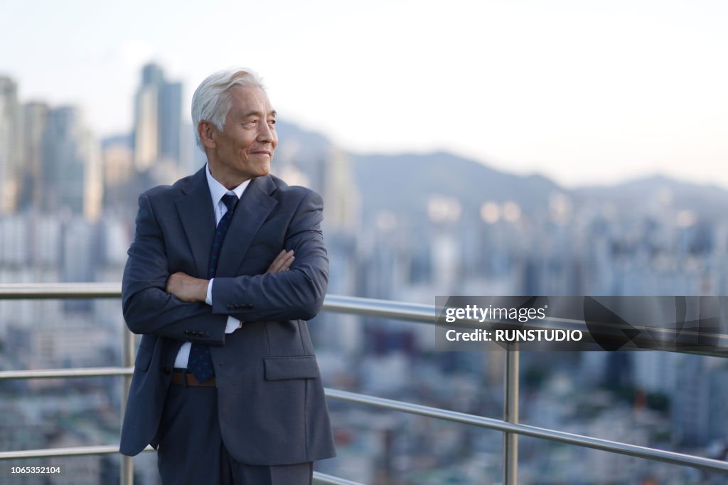 Senior businessman standing with arms crossed on rooftop