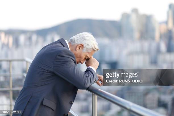 thoughtful senior businessman leaning on balcony railing - work japan stock pictures, royalty-free photos & images