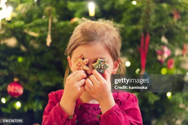 girl is holding star cookies in front of her eyes at christmas time - kids advent stock pictures, royalty-free photos & images
