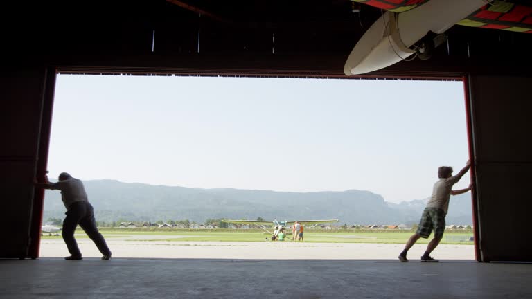 https://media.gettyimages.com/id/1065392248/video/two-men-opening-the-door-of-the-hangar-at-the-airport-and-revealing-a-sunny-airport.jpg?b=1&s=640x640&k=20&c=Fj563UxXCXfZb95Iqk1Xz3TVB3P12XPL-MkVR6OzW4A=