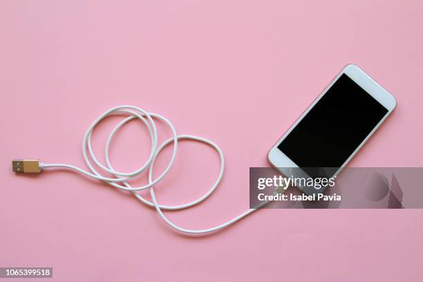 smart phone connected to usb cable on pink background - chargers stock-fotos und bilder