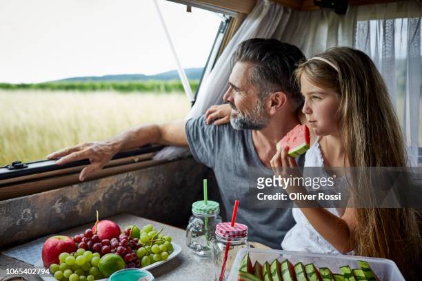 father with daughter eating watermelon in a caravan looking out of window - caravan holiday family imagens e fotografias de stock