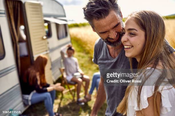 happy father with daughter on a field next to a caravan - familie jugendlicher zufrieden stock-fotos und bilder