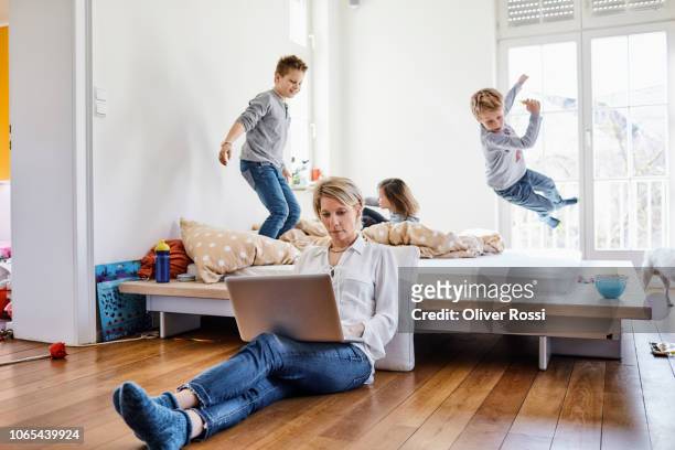 mother using laptop at home with children romping around in background - day 4 stock-fotos und bilder