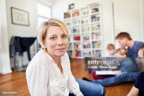 portrait of smiling woman sitting on the floor with family in background - focus on foreground stock pictures, royalty-free photos & images