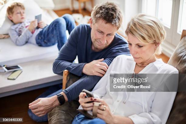 parents using cell phone with son lying on bed - distraído imagens e fotografias de stock