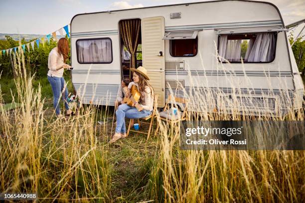 mother with two daughters sitting outside caravan playing guitar - camping trailer stock pictures, royalty-free photos & images