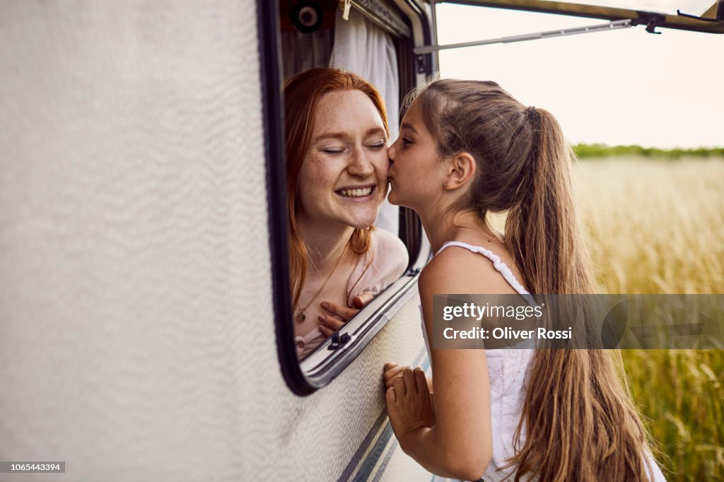 Girl kissing older sister through the window of a caravan