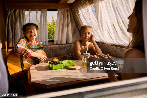 family sitting in caravan with fruit on table and girl holding guitar - caravan holiday family imagens e fotografias de stock