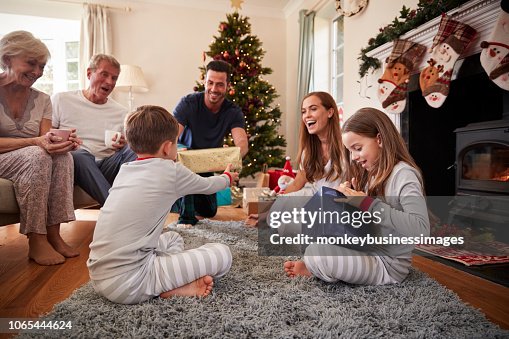 Three Generation Family Wearing Pajamas In Lounge At Home Opening Gifts On Christmas Day Three Generation Family Wearing Pajamas In Lounge At Home Opening Gifts On Christmas Day