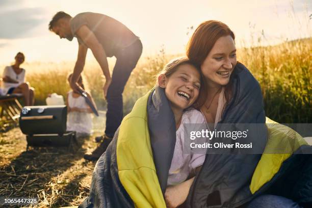 young woman and her younger sister wrapped in a sleeping bag in rural landscape - camping outdoors stock pictures, royalty-free photos & images