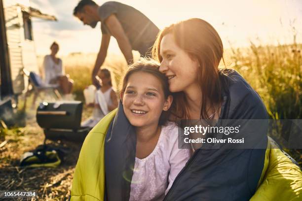 young woman and her younger sister wrapped in a sleeping bag in rural landscape - schwester stock-fotos und bilder