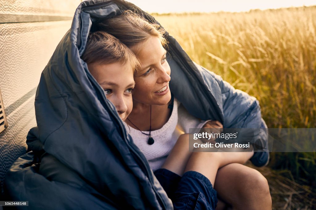 Mother and son sharing a sleeping bag at a caravan