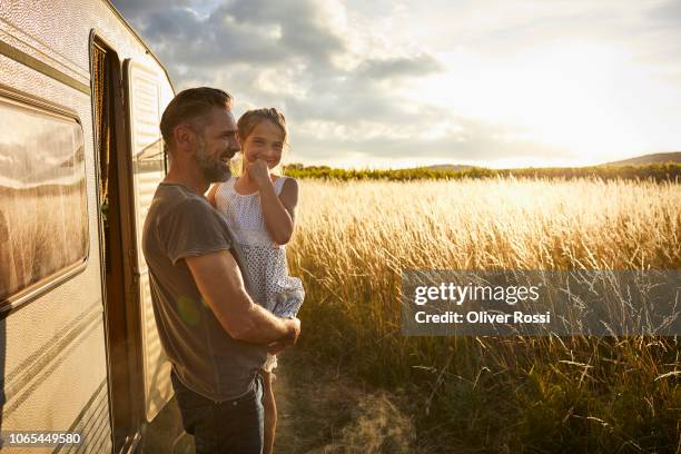 happy father holding daughter outside caravan in rural landscape - family caravan stock pictures, royalty-free photos & images