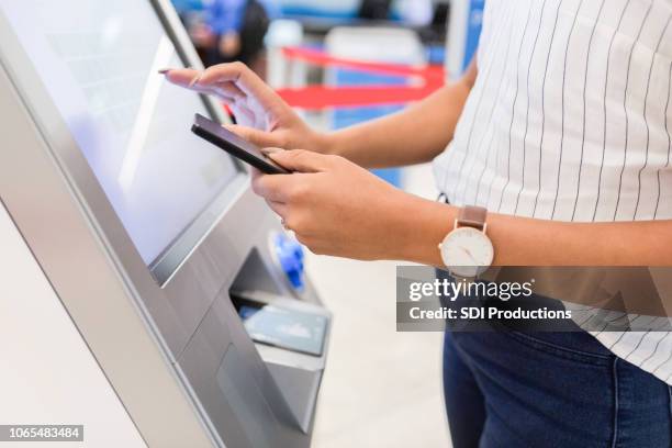 eine frau steht an einem kiosk in einem flughafen, als sie ihre gepäckanhänger bekommt - interactive kiosk stock-fotos und bilder