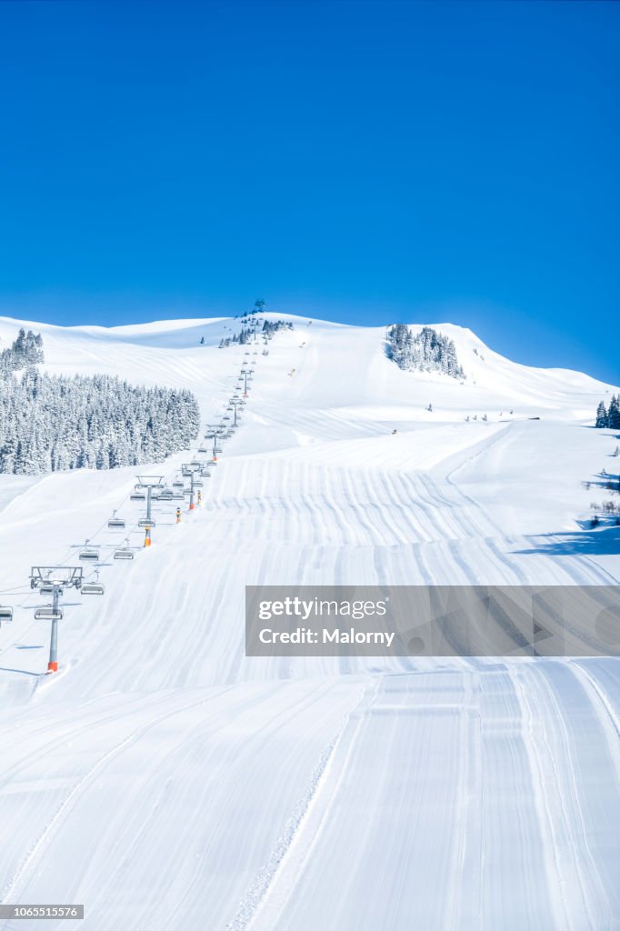 Untouched ski run with ski lift on the side, pristine snow and blue sky