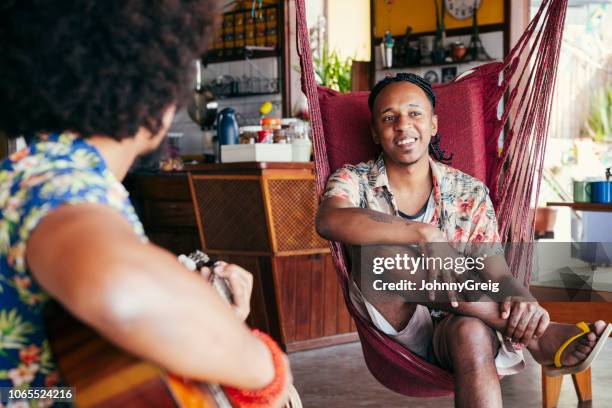 brazilian men relaxing, one playing guitar - young man listening music and relaxing in hammock stock pictures, royalty-free photos & images