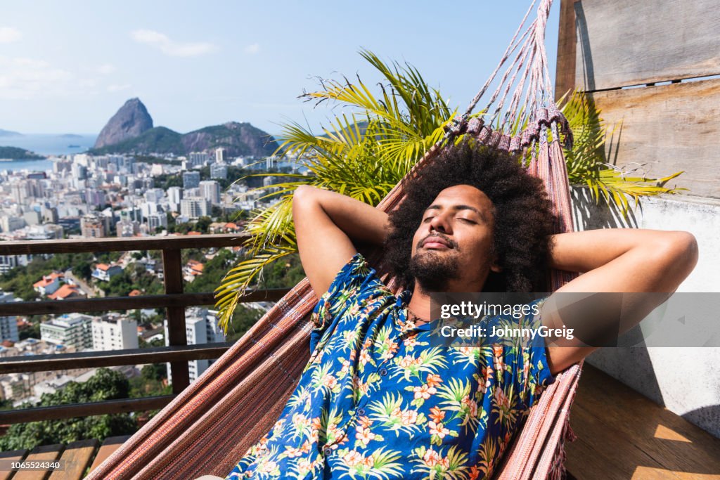 Brazilian man asleep on hammock, Sugar Loaf Mountain in distance