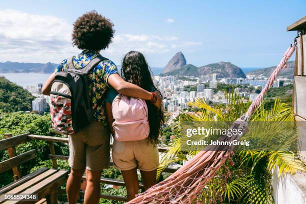rear view of two backpackers looking at view of sugar loaf mountain - vacation brazil rio de janeiro stock pictures, royalty-free photos & images