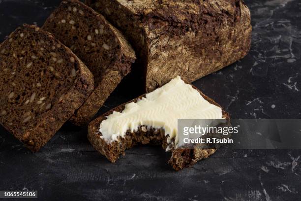rye black bread with seeds and butter on dark board background - rye grain foto e immagini stock