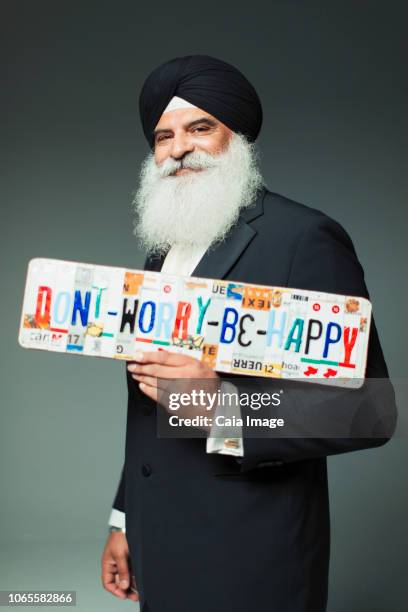 portrait smiling, well-dressed senior man in turban holding  dont worry be happy  license plates - sikh fotografías e imágenes de stock