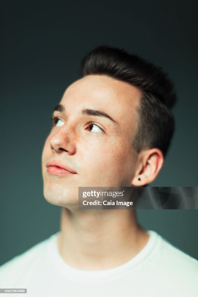 Portrait thoughtful teenage boy with freckles and earring looking up