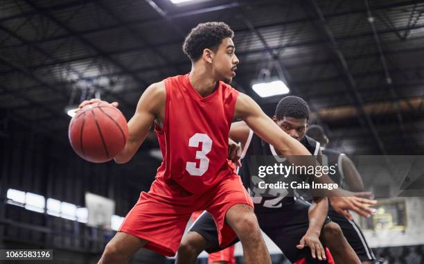 young male basketball player dribbling the ball, playing game in gymnasium - collegiate defensive player stock pictures, royalty-free photos & images