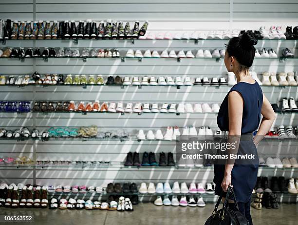 woman shopping looking at shelves of shoes - schoenenwinkel stockfoto's en -beelden