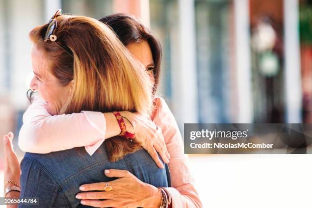 two mature hispanic female friends in full embrace as they reunite - reunite stock pictures, royalty-free photos & images