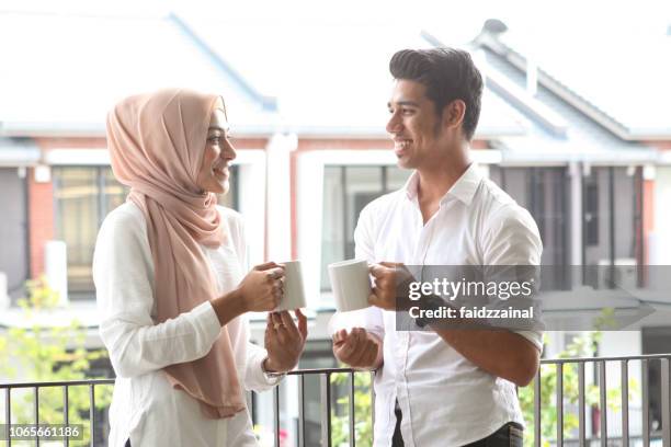 a young malay muslim couple having a drink by a balcony - malay couple stock pictures, royalty-free photos & images