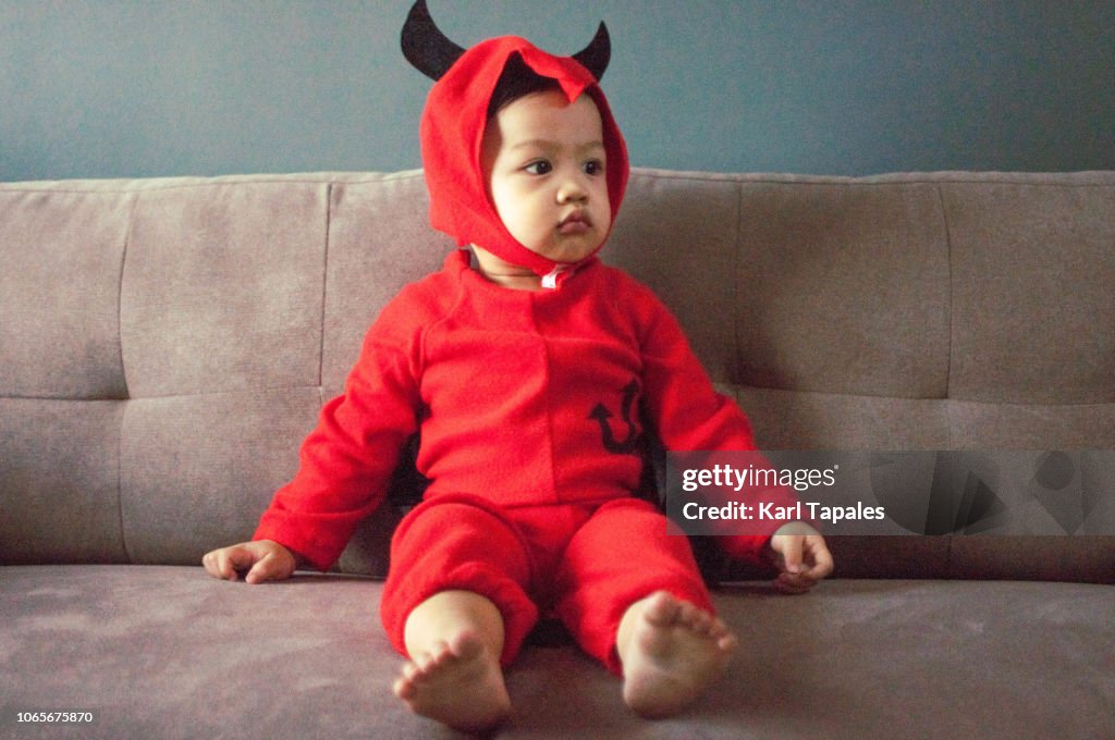 A baby boy in red devil's costume with tail and horns