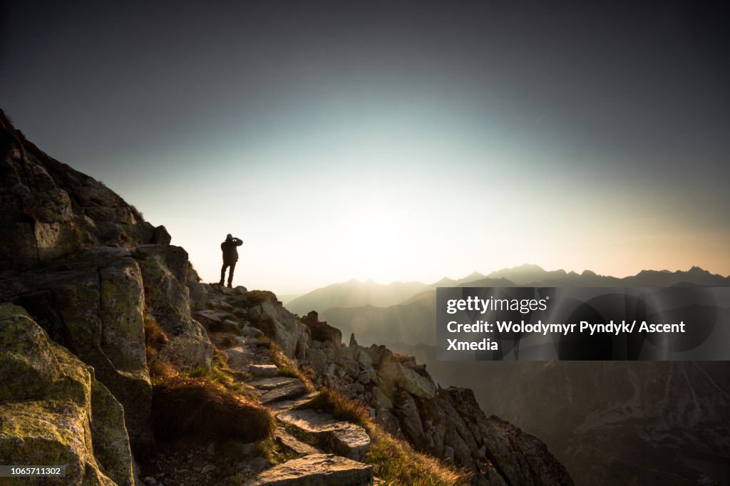 Man hiker standing on ridge and overlooking mountain valley