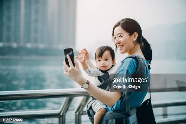 Mother and cute baby girl taking selfie joyfully with smartphone by the harbour in city
