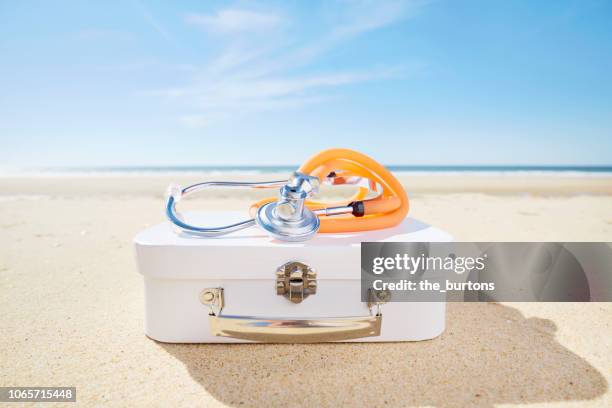 stethoscope and suitcase on beach by the sea, symbol for travel pharmacy/ first aid kit - kit imagens e fotografias de stock