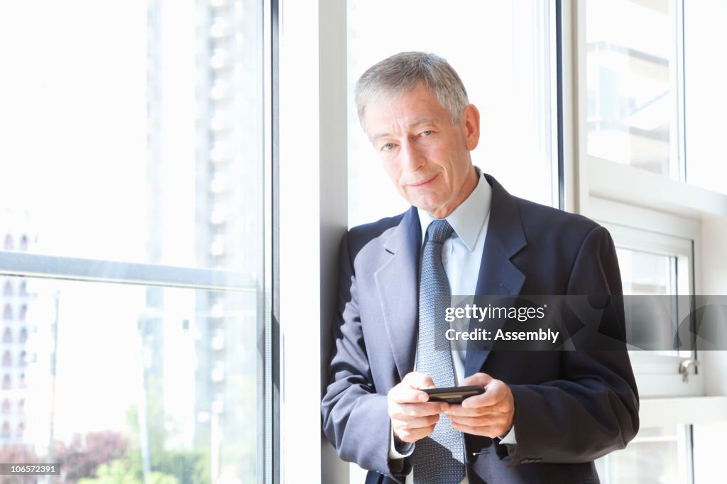 Mature businessman texting in office, portrait