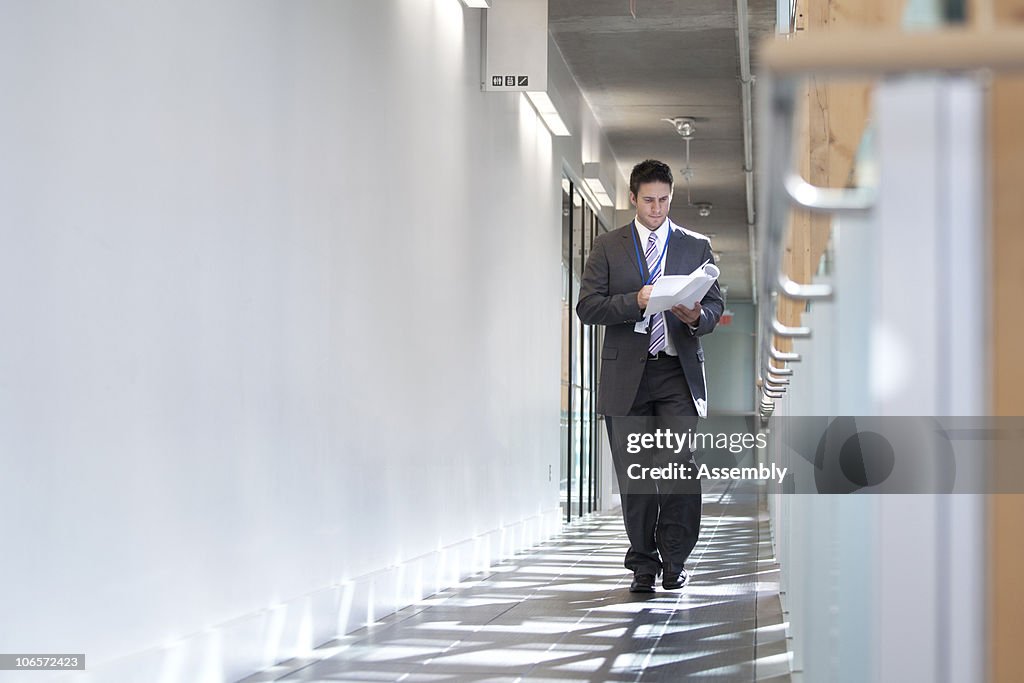 Businessman walking down hallway reading documents